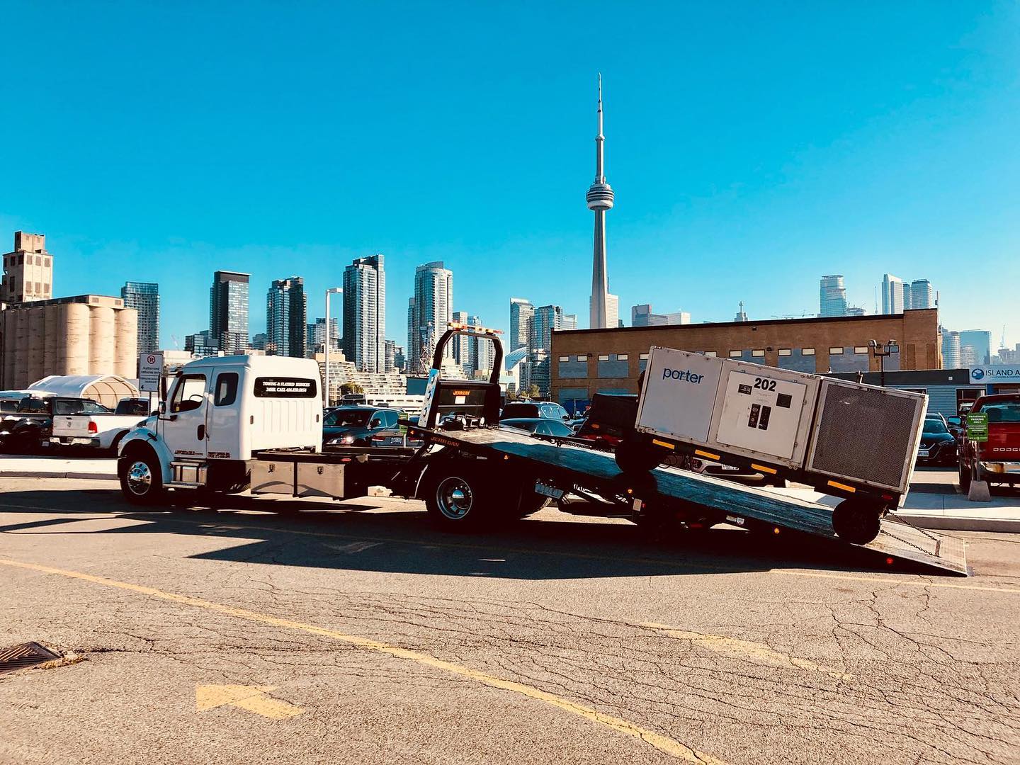 Flatbed truck loading equipment on a tilted deck in front of the Toronto skyline and CN Tower