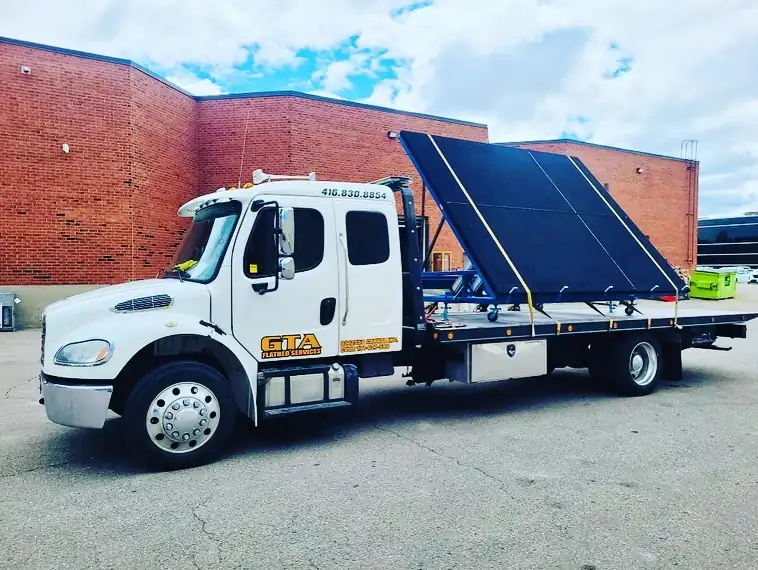 Tilt deck truck carrying a large black panel