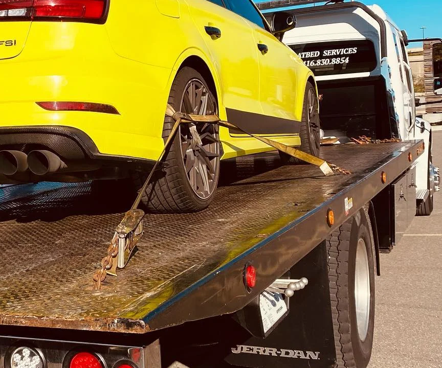 Soft strap over the rear wheel of a yellow Audi on a flatbed deck